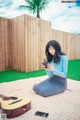 A woman sitting on a blanket with a guitar and a cell phone.