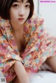 A woman in a colorful kimono sitting on a bed.