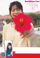 A woman holding a red flower in front of her face.