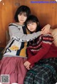 A couple of young women sitting next to each other on a bed.