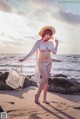 A woman in a white bikini and straw hat on the beach.