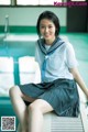 A woman in a school uniform sitting on the edge of a pool.