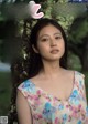 A woman in a floral dress standing in front of a tree.