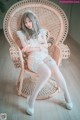 A woman sitting in a wicker chair wearing white lingerie.