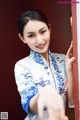 A woman in a blue and white cheongsam leaning against a wall.