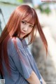 A woman with long red hair leaning against a wall.